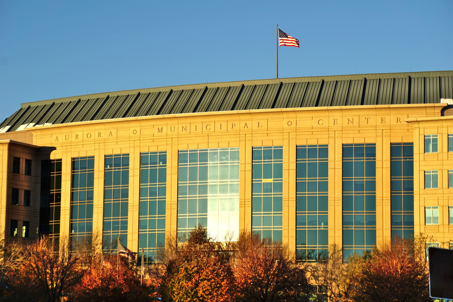 Aurora Municipal Center building with waving American flag in daylight.